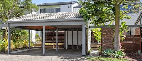 A covered outdoor area with a paved floor, a wooden fence, and a tree.