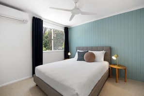 A bedroom with a bed, a ceiling fan, a window with curtains, and a nightstand with a lamp. - Villa Le Miramar Perfect for your Pooch Holiday (Noosa)
