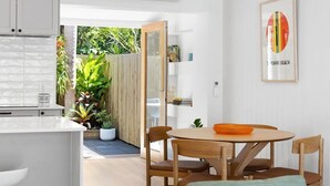 A modern kitchen with white cabinets, a dining area with wooden chairs, and a framed picture on the wall. - Villa Le Miramar Perfect for your Pooch Holiday (Noosa)