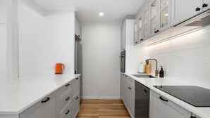 A narrow kitchen with white cabinetry, a wooden floor, and a stainless steel dishwasher. - Villa Le Miramar Perfect for your Pooch Holiday (Noosa)