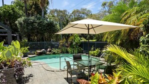 A swimming pool with a glass table and chairs, surrounded by lush greenery and a fence. - Villa Le Miramar Perfect for your Pooch Holiday (Noosa)