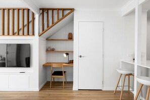 A modern interior with a wooden staircase, a desk with a chair, a television, and a white door. - Villa Le Miramar Perfect for your Pooch Holiday (Noosa)