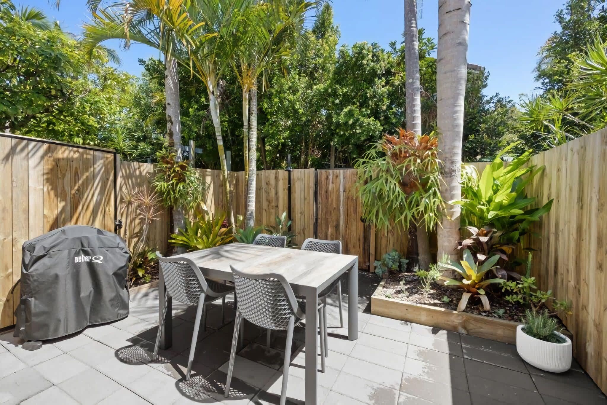An outdoor patio with a table and chairs, a grill, and a wooden fence.