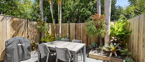 An outdoor patio with a table and chairs, a grill, and a wooden fence.