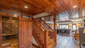 A spacious interior with a wooden staircase, stone wall, and a dining area with chairs and tables.
