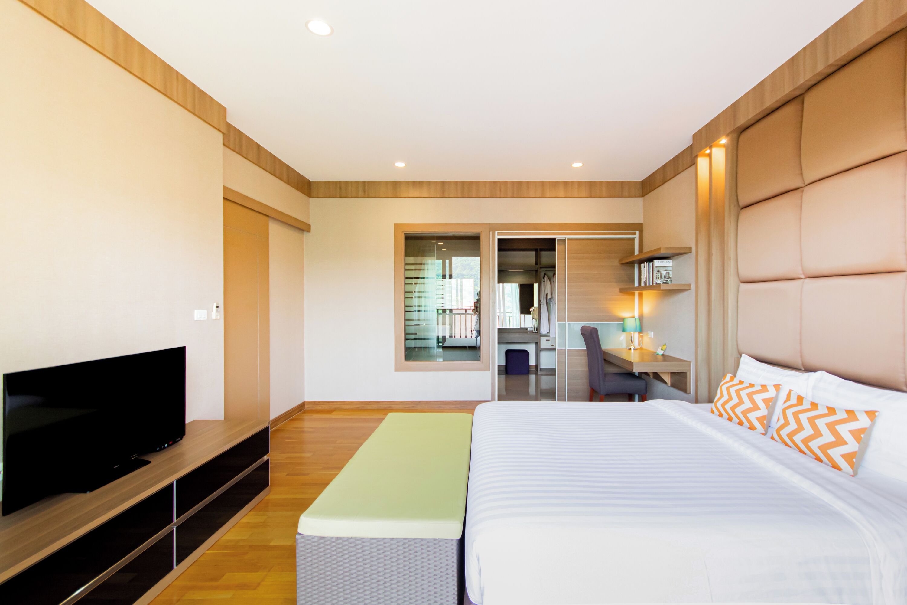 A modern hotel room with a large bed, a flat-screen TV, a desk, and a view of the hallway.