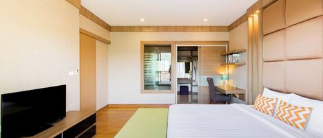 A modern hotel room with a large bed, a flat-screen TV, a desk, and a view of the hallway.