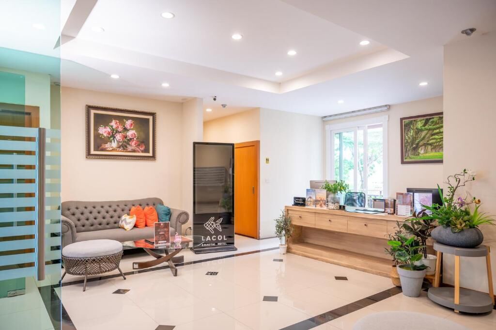 A modern hotel lobby with a sofa, a coffee table, a reception desk, and potted plants.