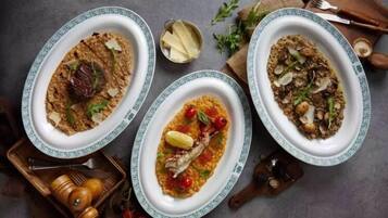 Three oval dishes with food, a pepper grinder, and a small bowl of cheese on a table.