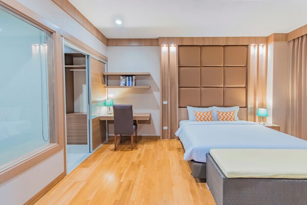 Ein modernes Hotelzimmer mit Holzboden, Schreibtisch und Stuhl, einem Bett mit Kissen, einem Kleiderschrank und einem Regal mit Büchern.