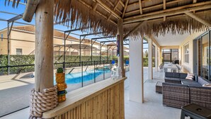 A covered outdoor area with a pool, wooden seating, and a bar. - Mini Golf, Arcade, Huge Bedroom w/ Slide, Waterpark, Tiki Bar: Imagination Station (Davenport)