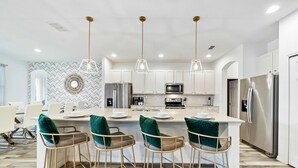 A modern kitchen with white cabinets, stainless steel appliances, and a central island with bar stools. - Mini Golf, Arcade, Huge Bedroom w/ Slide, Waterpark, Tiki Bar: Imagination Station (Davenport)