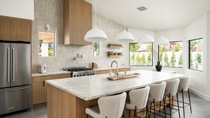Una cocina moderna con una isla grande, electrodomésticos de acero inoxidable e iluminación colgante.