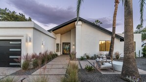 Una casa moderna con garaje, un porche cubierto y un patio con mobiliario exterior.