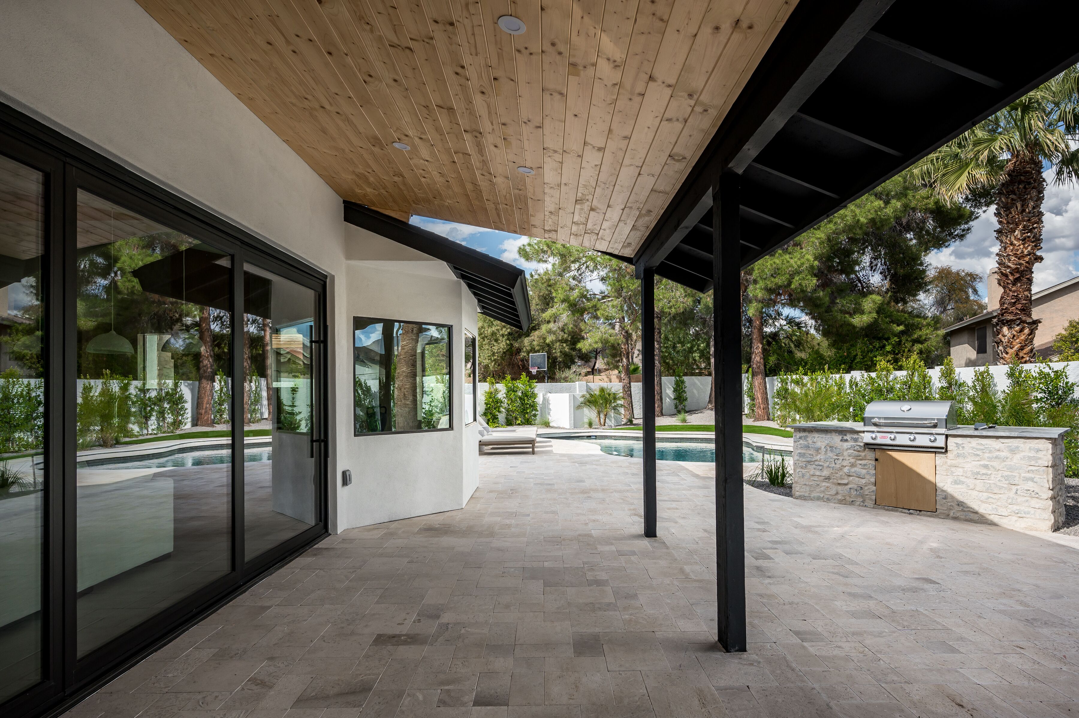 Patio esterno moderno con piscina, zona barbecue e area salotto coperta.