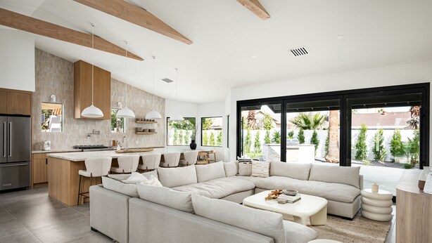 Una cocina moderna con una isla central, un comedor con sillas, un sofá grande en forma de L y vistas al exterior.