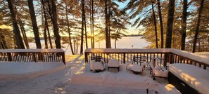 A snow-covered deck with benches and a railing overlooking a lake.