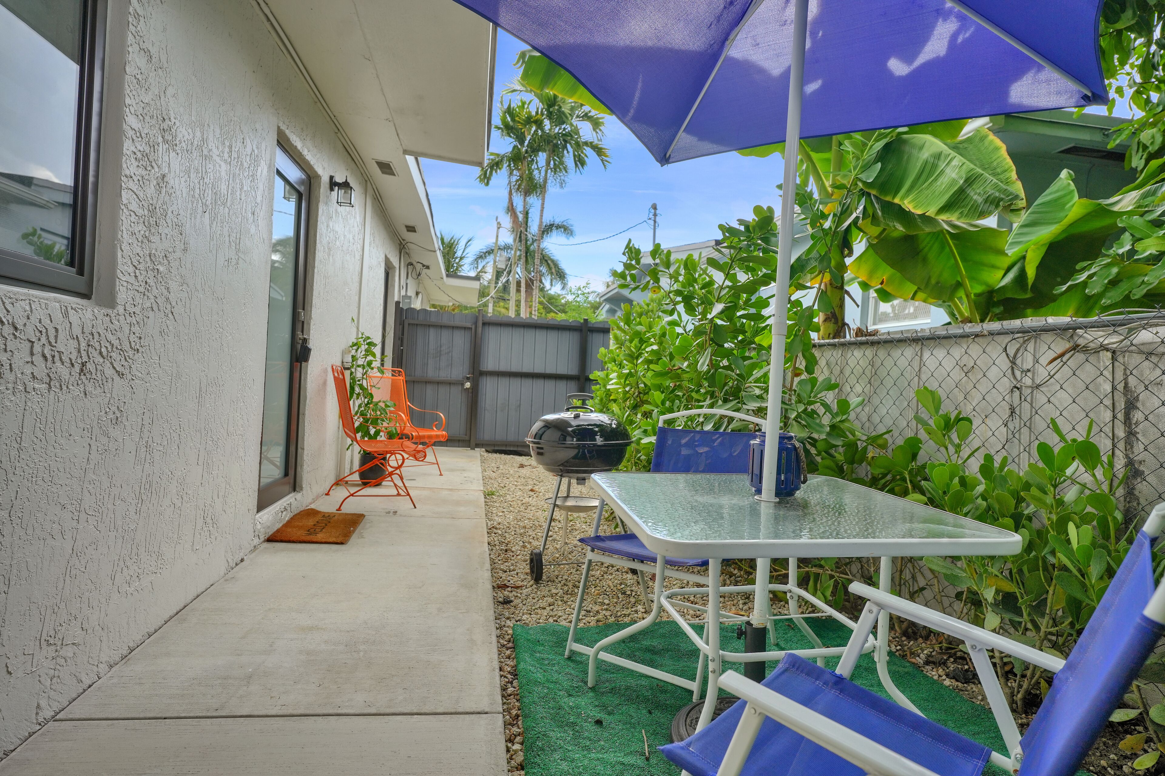 Une terrasse avec une table et des chaises, un barbecue et un parasol bleu.