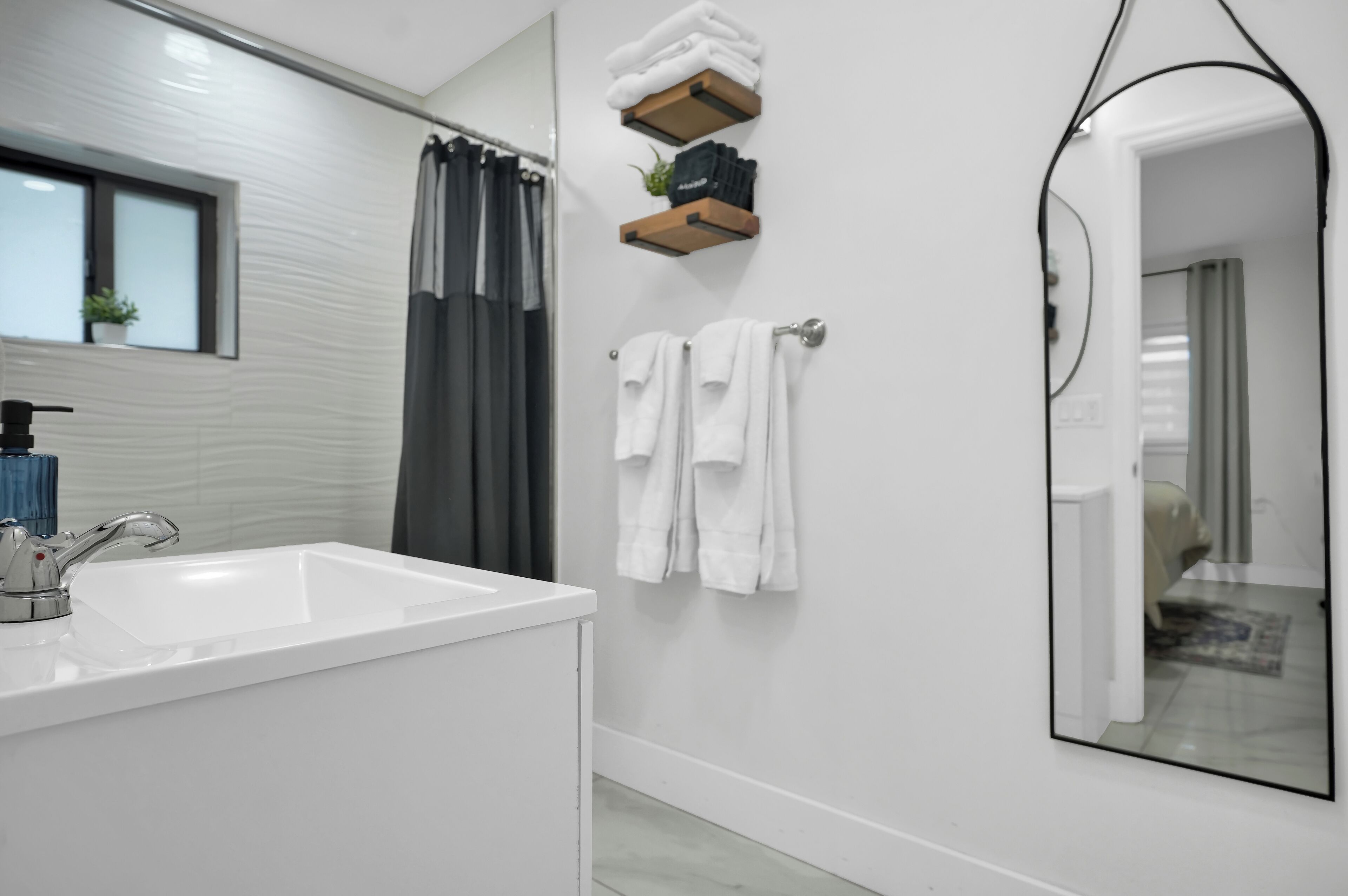 A modern bathroom with a white sink, a mirror, and a shower area.