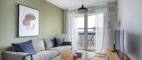 A modern living room with a grey sofa, a round coffee table, and a TV on a wooden stand.