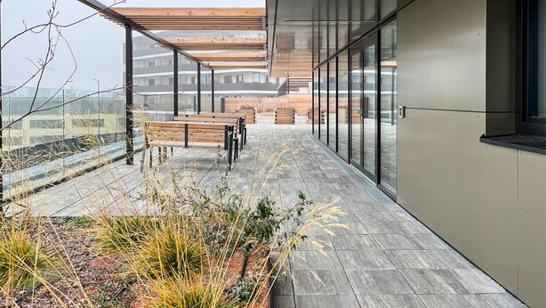 Une terrasse extérieure moderne, dotée de bancs en bois, de murs en verre et offrant une vue sur le paysage urbain.