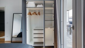 Une chambre moderne dotée d’un grand lit, d’un dressing avec étagères et espace pour suspendre les vêtements, et d’une porte-fenêtre coulissante donnant sur un balcon.