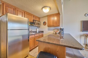 Una cocina con armarios de madera, un refrigerador de acero inoxidable, un microondas y una encimera de granito.