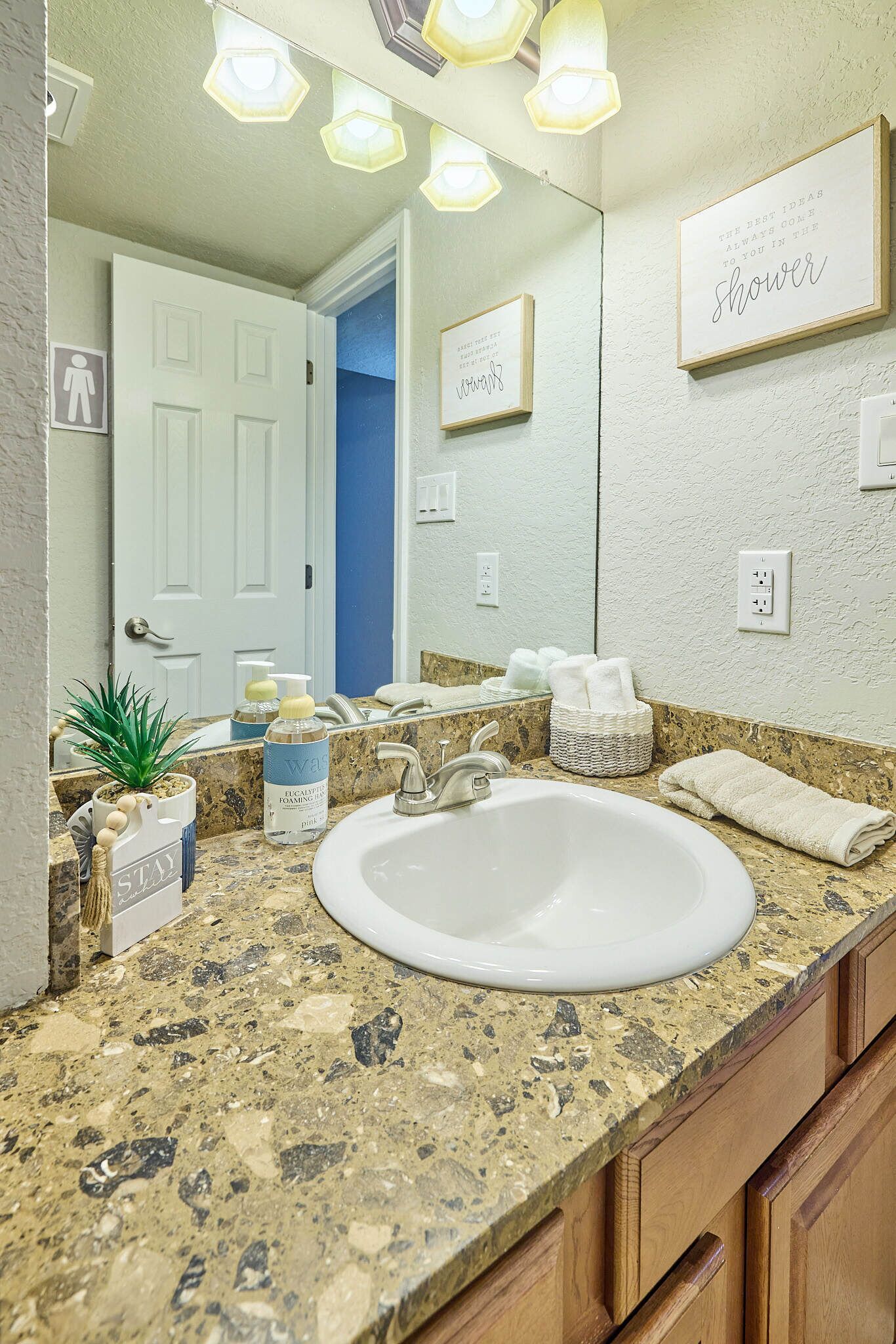 Un baño con encimera de granito, lavabo blanco y espejo encima. Hay toallas y artículos de aseo en la encimera.