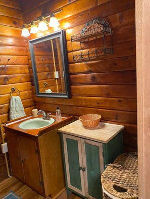 Ein Badezimmer einer Holzhütte mit Waschbecken, Spiegel und einem kleinen Tisch mit einem Korb.
