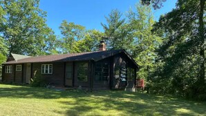 A rustic cabin with a sloped roof, a chimney, and a porch. - Quiet Log Cabin with private river access and hot tub (Great Cacapon)