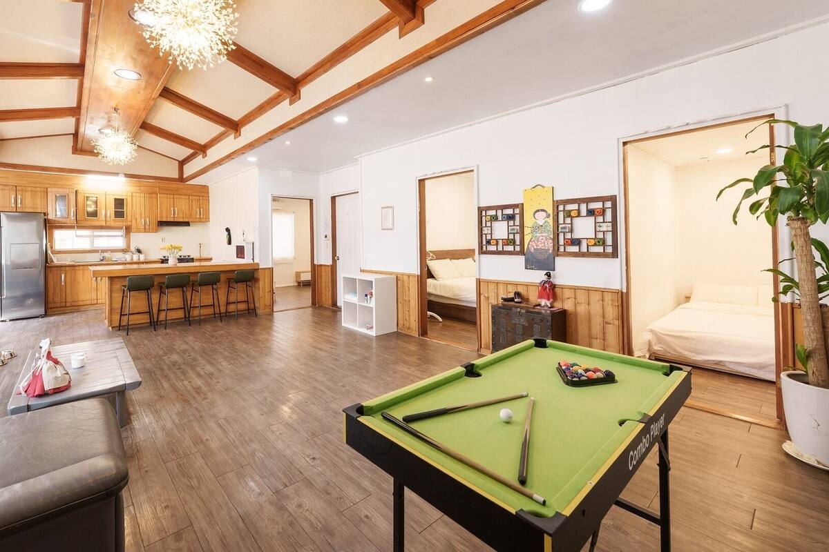 Een moderne woonkamer met een pooltafel, een bank en een keuken met houten kasten en een koelkast.