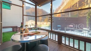 A covered outdoor patio with a round table, chairs, a bottle of wine, and a decorative lantern. - Gapyeong Jmong Choncance&camping Pension (Gapyeong)
