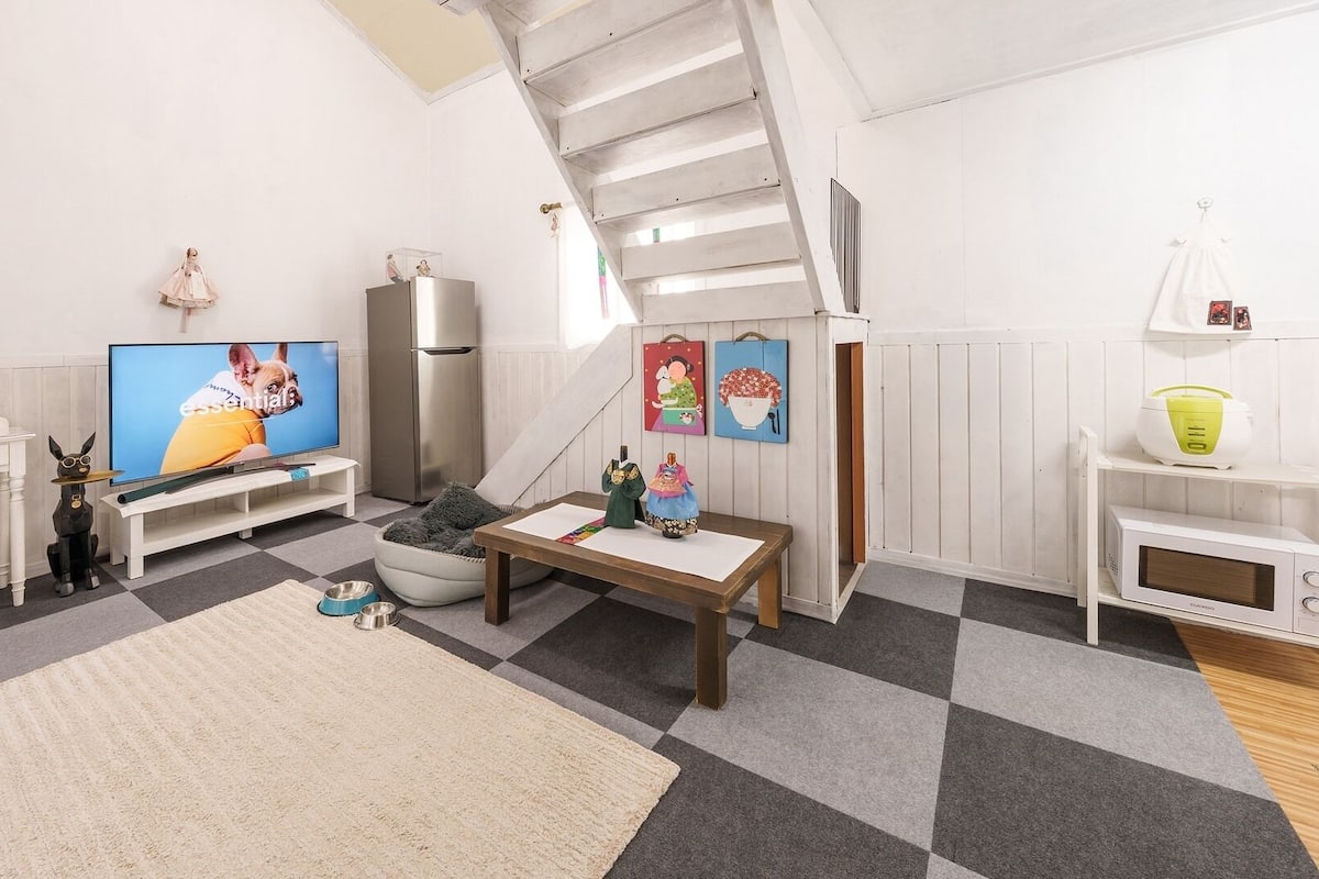 Een woonkamer met een televisie, bank, salontafel en een trap.