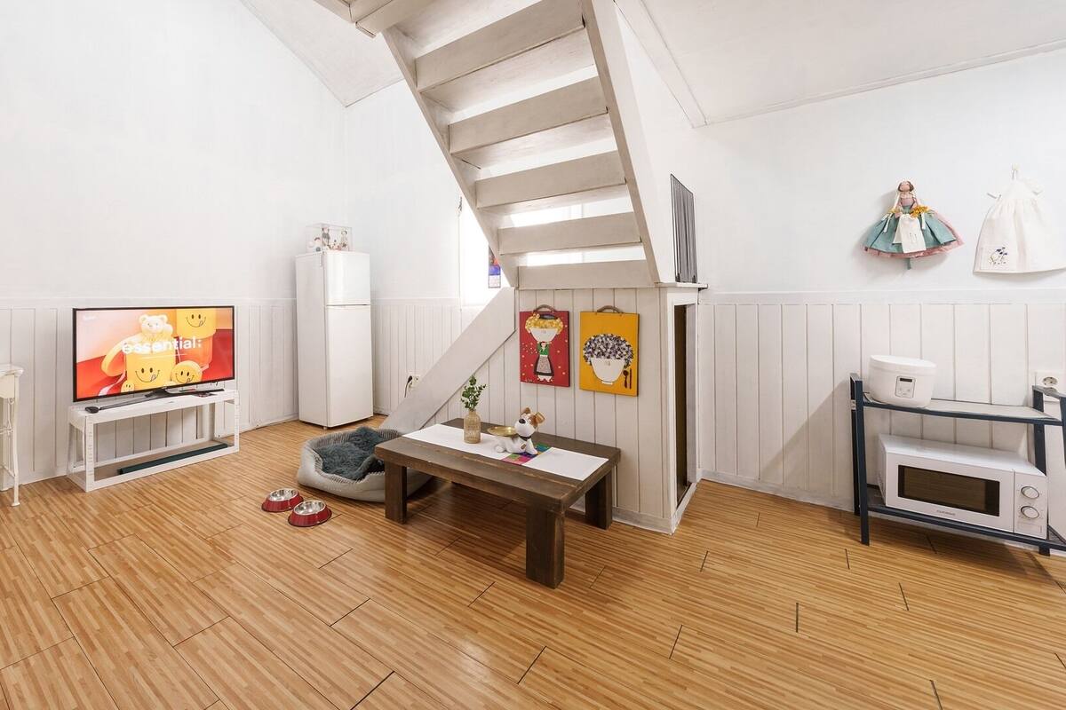 Een gezellige woonkamer met een televisie, een eettafel, een dierenbedje en een trap.