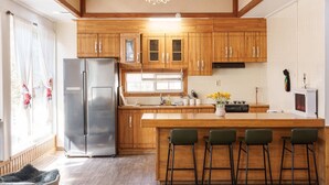 A kitchen with wooden cabinets, a stainless steel refrigerator, a bar area with stools, and a window with curtains. - Gapyeong Jmong Choncance&camping Pension (Gapyeong)