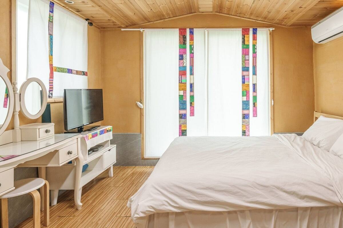 Een slaapkamer met een bed, een televisie, een dressoir en een spiegel.