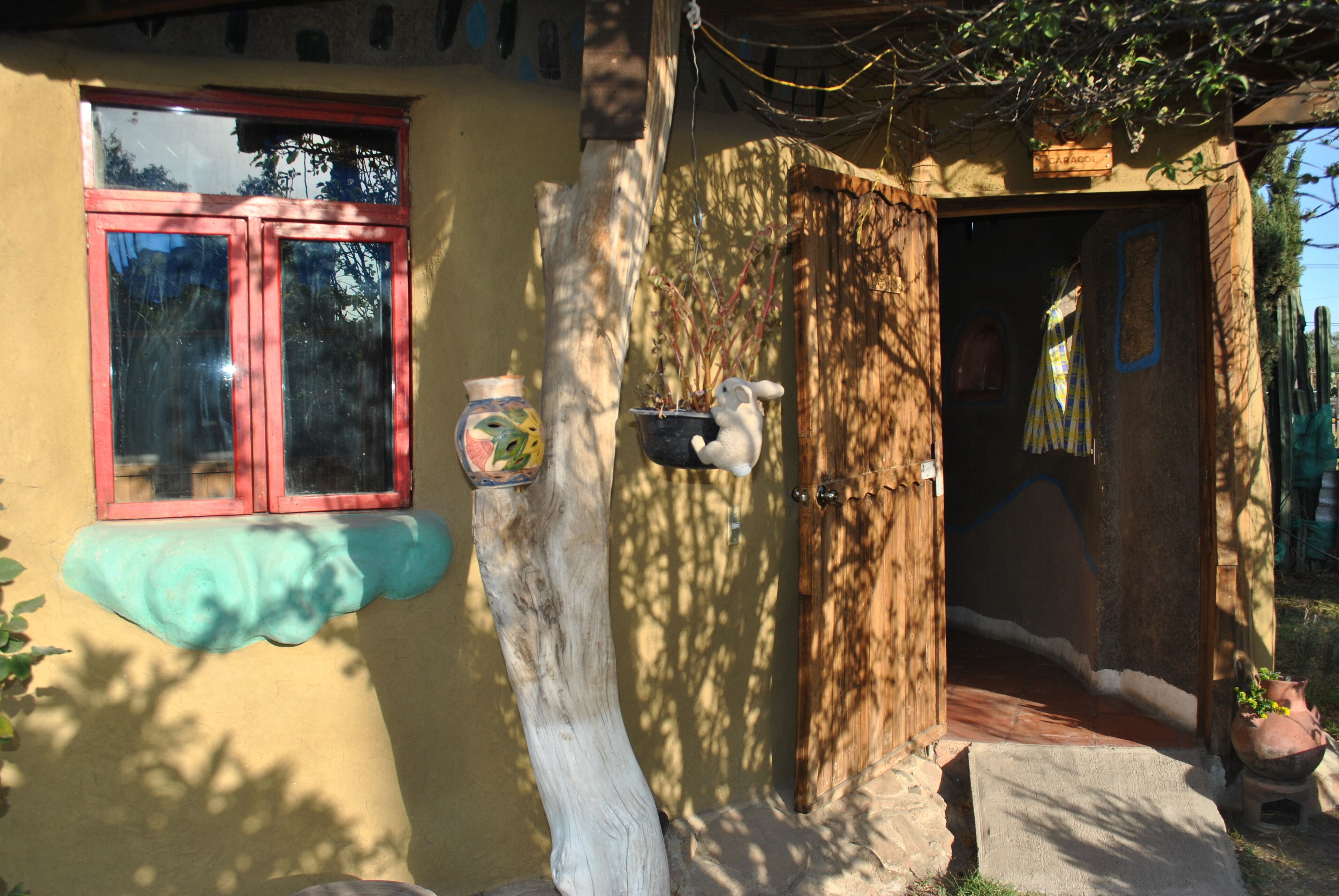 A rustic building with a wooden door, a window with red trim, and a small porch area with a potted plant.