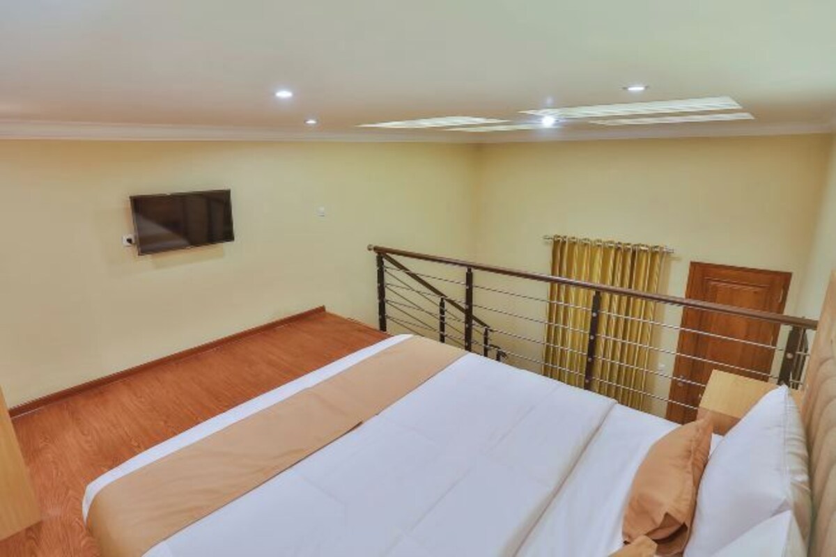 Une chambre d’hôtel avec un lit, un téléviseur fixé au mur, un plancher en bois et une fenêtre avec des rideaux.