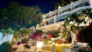 Un immeuble à plusieurs étages doté de balcons, entouré d’une végétation luxuriante et de plantes en fleurs.