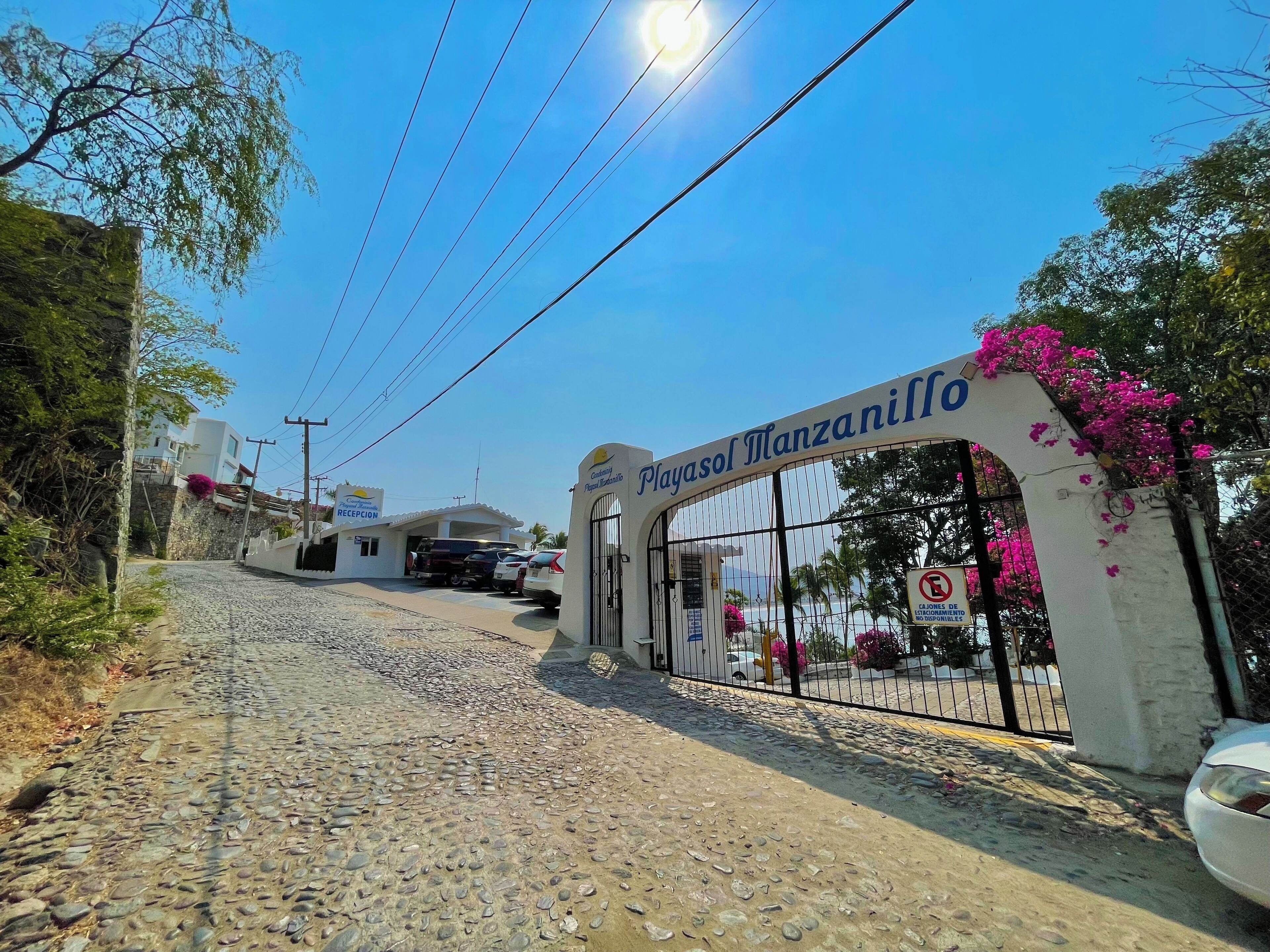 A stone-paved entrance to Playasol Manzanillo with a reception area and parked cars.