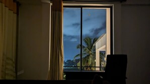 A hotel room with a bed, a window with curtains, and a view of palm trees and a building.