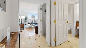 A hallway with a wooden reception desk, a view of a cityscape through large windows, and a door leading to a bathroom. - Two Beachfront Stylish CozySuites  (Atlantic City)