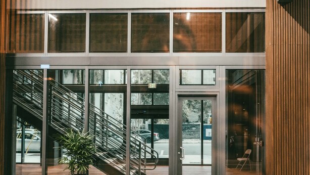 Una entrada moderna de edificio con puerta de cristal, escaleras y plantas en macetas.