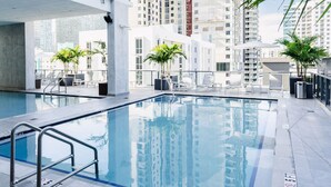 Un área de piscina en la azotea con agua azul cristalina, rodeada de edificios modernos y plantas en macetas.
