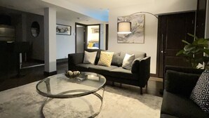 A modern living room with a glass coffee table, a dark sofa with patterned cushions, and a painting on the wall. - The Lux Den Speaks for itself. Cozy, bright self-contained basement suite  (Yorkton)