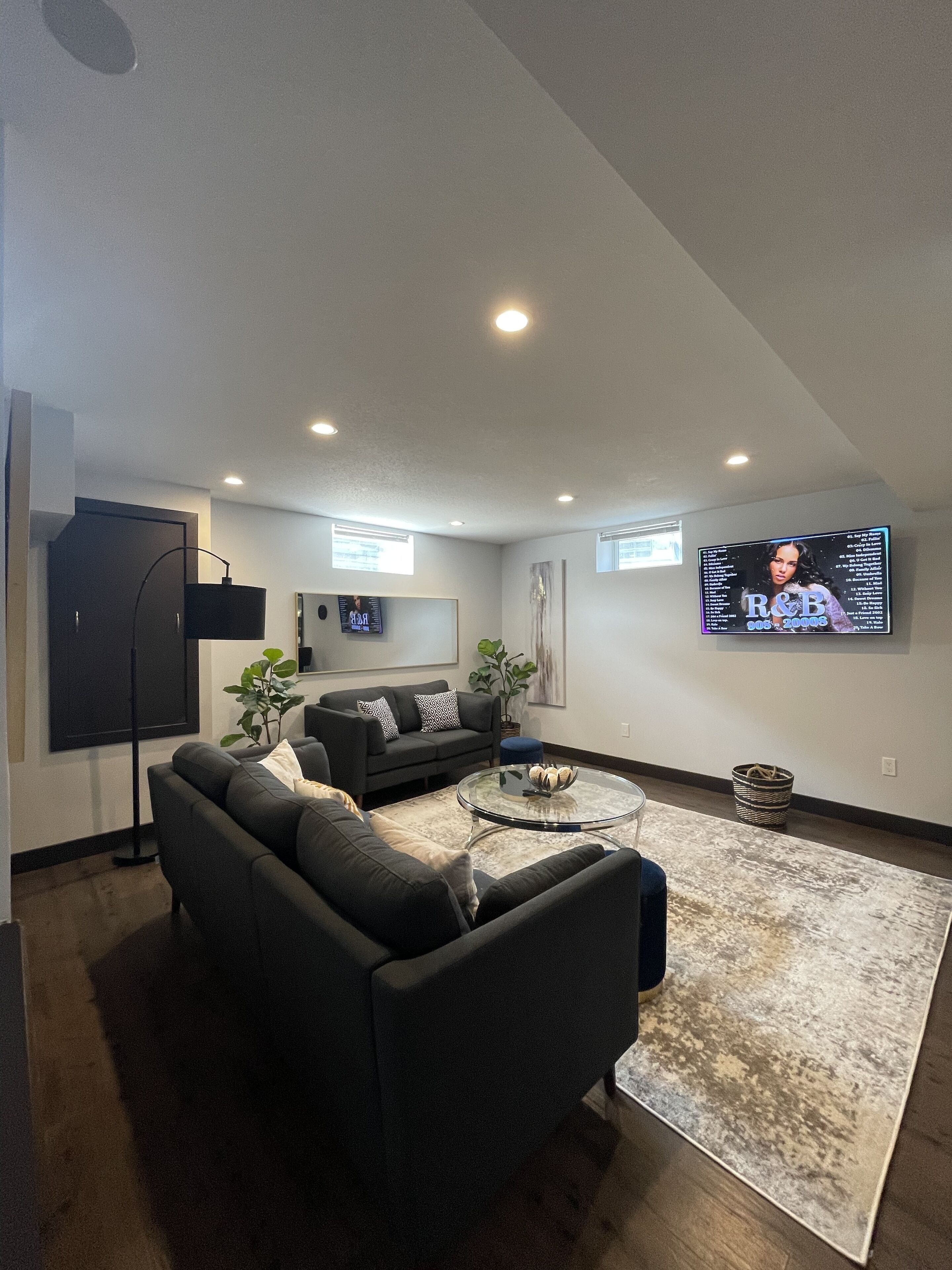 A modern living room with a sectional sofa, a coffee table, and a flat-screen TV mounted on the wall.