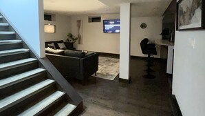 A modern interior with a staircase leading to a living area, a flat-screen TV mounted on the wall, and a small desk with a chair. - The Lux Den Speaks for itself. Cozy, bright self-contained basement suite  (Yorkton)