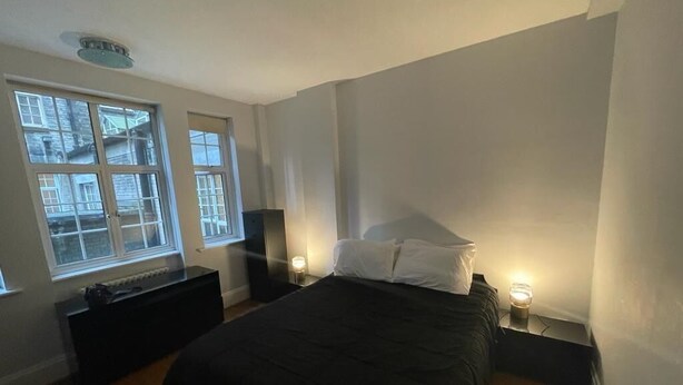 A bedroom with a large bed, two bedside tables with lamps, a dresser, and a window with a view of buildings. - 1 Bed Flat Sleeps 3 - Wifi, Near City Centre (London)