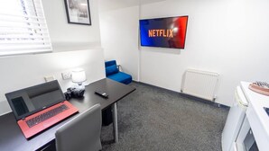 Une pièce avec un ordinateur portable posé sur un bureau, une chaise bleue, un radiateur blanc et un téléviseur affichant le logo de Netflix.