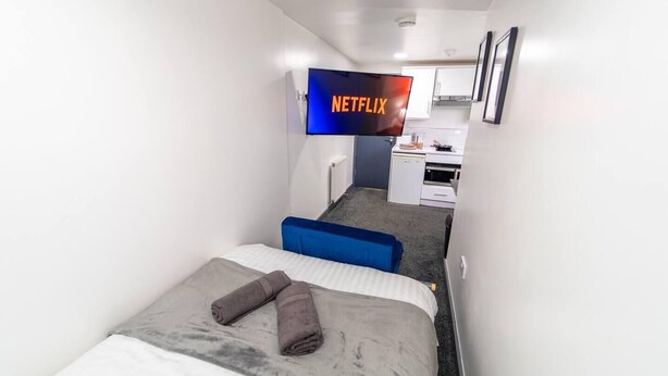 Une petite chambre d’hôtel moderne, équipée d’un lit, d’un bureau et d’une kitchenette.